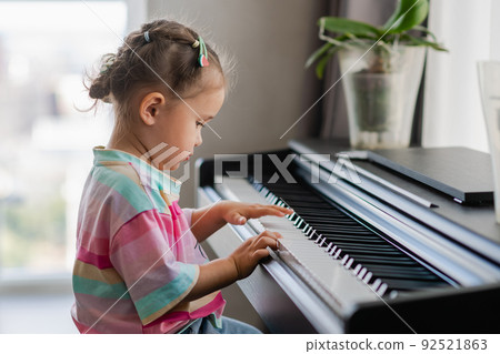 Side view of cute asian girl playing piano at home Side view of cute asian girl playing piano at home 92521863