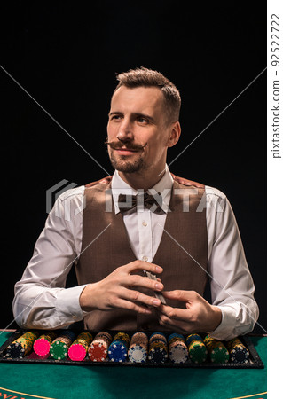 Portrait of a croupier is holding playing cards, gambling chips on table. Black background 92522722