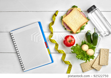 Healthy lunch in office at workplace or home. Whole-grain sandwich with ham and fresh vegetables and bottle of water. Top view, flat lay on wood Healthy lunch in office at workplace or home. Whole-grain sandwich with ham and fresh vegetables and bottle of water. Top view, flat lay on wood 92522750