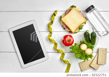 Sandwich, fresh vegetables, bottle of water and eggs on a table with a tablet, top view. Copy space Sandwich, fresh vegetables, bottle of water and eggs on a table with a tablet, top view. Copy space 92522751