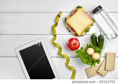 Sandwich, fresh vegetables, bottle of water and eggs on a table with a tablet, top view. Copy space Sandwich, fresh vegetables, bottle of water and eggs on a table with a tablet, top view. Copy space 92522753