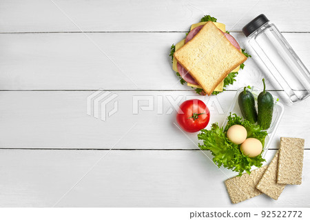 Healthy lunch box with sandwich, eggs and fresh vegetables, bottle of water on rustic wooden background. Top view with copy space Healthy lunch box with sandwich, eggs and fresh vegetables, bottle of water on rustic wooden background. Top view with copy space 92522772