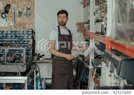 Man worker in uniform inspecting coffee machine in own workshop Man worker in uniform inspecting coffee machine in own workshop 92522809