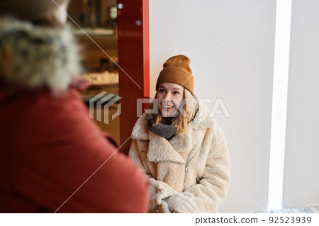 Horizontal over-the-shoulder shot of young Caucasian woman sitting outdoors on winter evening chatting with her boyfriend standing in front of her Horizontal over-the-shoulder shot of young Caucasian woman sitting outdoors on winter evening chatting with her boyfriend standing in front of her 92523939