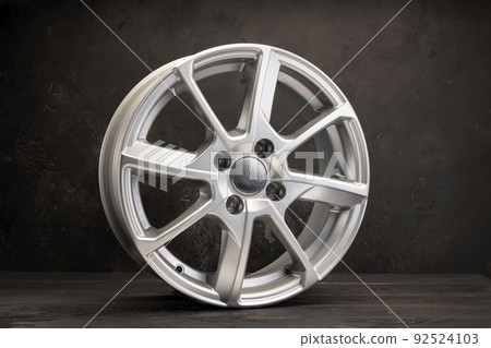 new grey alloy wheels on a dark textured black background. a wheel for a car new grey alloy wheels on a dark textured black background. a wheel for a car 92524103