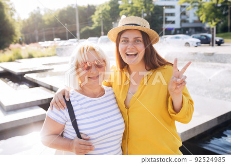 Positive beautiful womans looking at camera. Happy Redhead girl with mother walking on city street in a warm sunny day. Urban lifestyle concept. Travelers, summer time 92524985