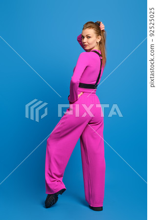 Young woman in purple knitted suit half turned back and put a leg on tiptoe over blue studio background 92525025