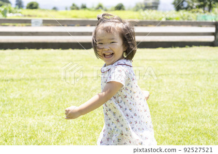 一個蹣跚學步的孩子帶著微笑在草地公園裡跑來跑去 一個蹣跚學步的孩子帶著微笑在草地公園裡跑來跑去 92527521