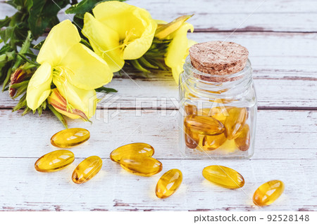 Evening primrose oil gel capsules in glass bottle, pills and yellow flowers on wooden table Evening primrose oil gel capsules in glass bottle, pills and yellow flowers on wooden table 92528148