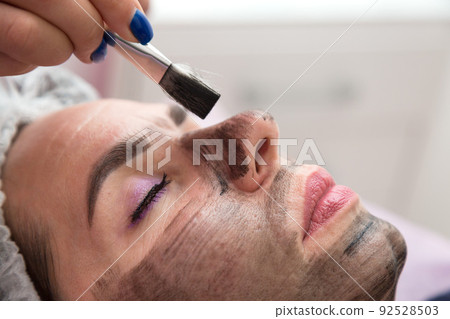 Portrait of an adult woman with her eyes closed during a carbon peeling procedure with a black mask on her face Portrait of an adult woman with her eyes closed during a carbon peeling procedure with a black mask on her face 92528503