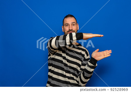 Cheerful hispanic man measuring invisible object with his hands, happy man holding something in arms while standing isolated on background, recommending new item, copy space. Cheerful hispanic man measuring invisible object with his hands, happy man holding something in arms while standing isolated on background, recommending new item, copy space. 92528969