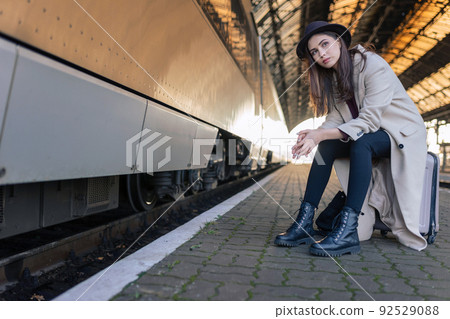 Lonely pensive woman sitting on the suitcase waiting for a train Lonely pensive woman sitting on the suitcase waiting for a train 92529088