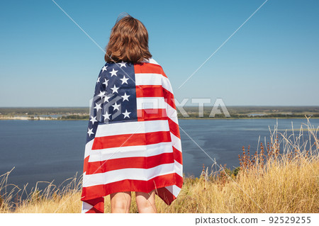 Young happy woman with usa flag enjoying the sunset in nature. View from the back. Young happy woman with usa flag enjoying the sunset in nature. View from the back. 92529255