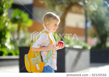 Little schoolboy joyfully goes to school after holiday. Child in a yard of schoolhouse. Education for children. Kids back to school concept. 92529588