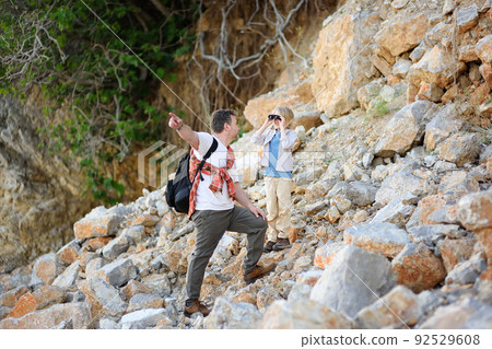 Cute schoolchild and his mature father hiking together on mountain and exploring nature. Child looking with a binoculars. 92529608