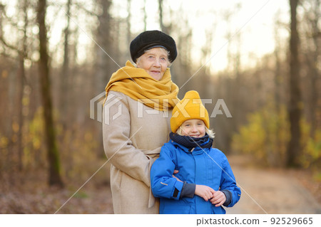 Little grandson and elderly grandmother during walking in autumn park. Friendship granny and grandchild. 92529665