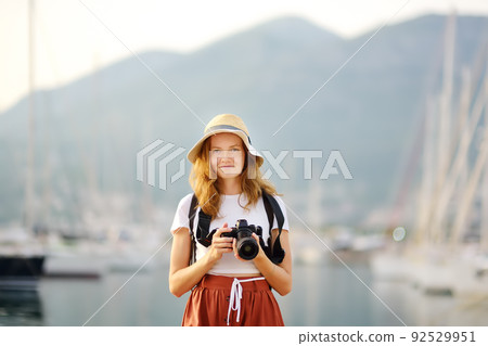 Charming young tourist woman taking a picture on the Mediterranean coast. Attractive red-haired girl photographer with a camera on the background of sea and yachts. 92529951