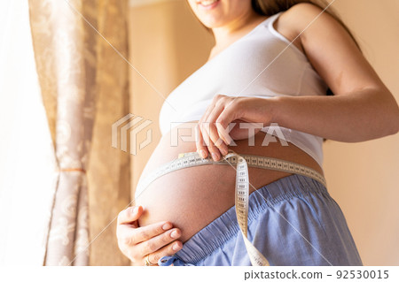 Belly size pregnancy woman measure. Happy young pregnant woman with tape measuring belly. Therapy, healthcare, motherhood concept. Belly size pregnancy woman measure. Happy young pregnant woman with tape measuring belly. Therapy, healthcare, motherhood concept. 92530015