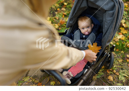 Mather while walking in the autumn park, shows the baby in the stroller orange leaf Mather while walking in the autumn park, shows the baby in the stroller orange leaf 92530042