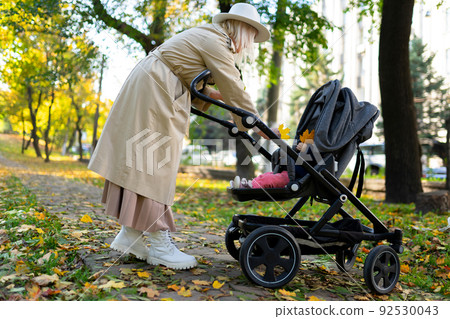 Mother with baby pram walking in autumn park Mother with baby pram walking in autumn park 92530043