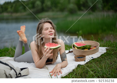 Girl relaxing and eat watermelon outdoor near lake. Picnic in nature  92530238