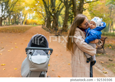 Mom kisses her baby while holding in arms while walking in the park Mom kisses her baby while holding in arms while walking in the park 92530306