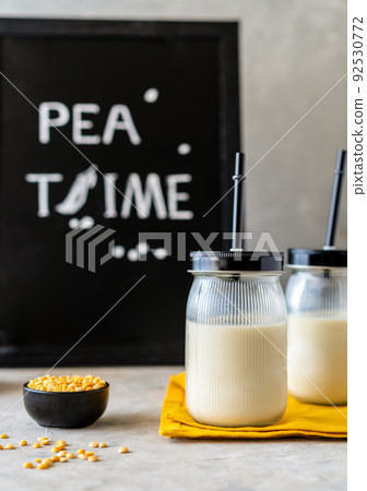 Vegan healthy pea milk in glass jars with drinking straws, concrete background, pea grains and mockup place 92530772