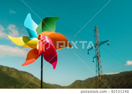 Close-up multi-colored pinwheel and electric power line against the background of green mountains and sky. 92531148