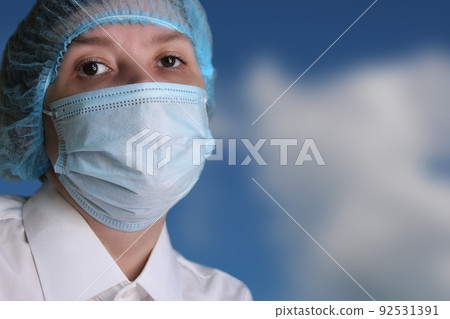 Close-up portrait of a woman doctor in a medical cap and mask against the blue sky.. 92531391