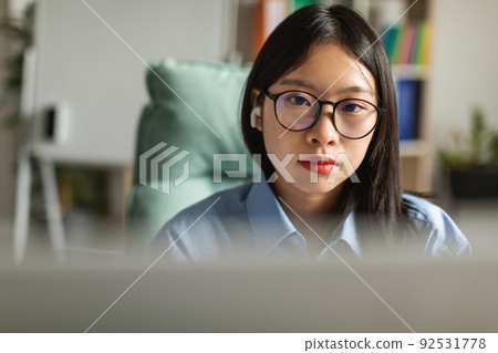 Japanese Business Female Wearing Earbuds Using Computer At Workplace Indoor Japanese Business Female Wearing Earbuds Using Computer At Workplace Indoor 92531778
