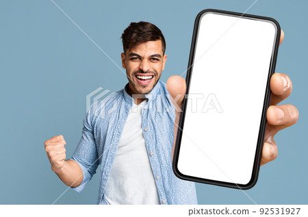 Excited guy shakes clenched fist and showing cell phone, mockup Excited guy shakes clenched fist and showing cell phone, mockup 92531927