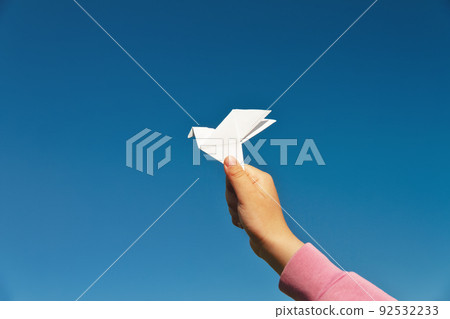white paper origami pigeon in children's hand on blue sky background 92532233
