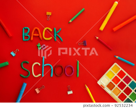 words of multi-colored plasticine back to school and school supplies felt-tip pens, paints, pen, paper clips, on red background top view 92532234