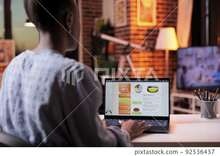 Corporate worker analyzing diagrams and charts with company marketing research, looking on laptop screen in home office in evening. Business research results data on computer Corporate worker analyzing diagrams and charts with company marketing research, looking on laptop screen in home office in evening. Business research results data on computer 92536437