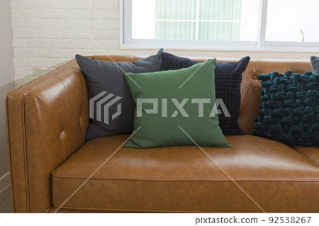 Light modern living room with brown leather couch and white, grey and green pillow on it. Light modern living room with brown leather couch and white, grey and green pillow on it. 92538267