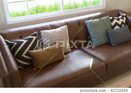 Light modern living room with brown leather couch and white, grey and green pillow on it. Light modern living room with brown leather couch and white, grey and green pillow on it. 92538269