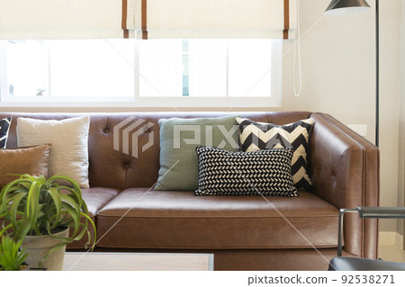 Light modern living room with brown leather couch and white, grey and green pillow on it. Light modern living room with brown leather couch and white, grey and green pillow on it. 92538271