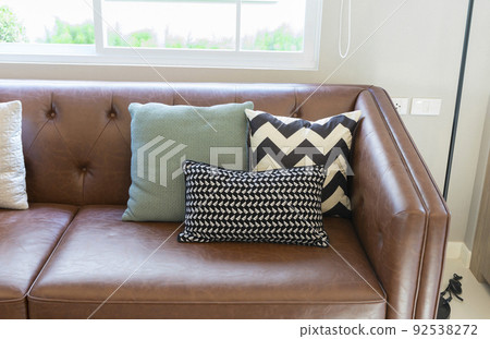 Light modern living room with brown leather couch and white, grey and green pillow on it. Light modern living room with brown leather couch and white, grey and green pillow on it. 92538272