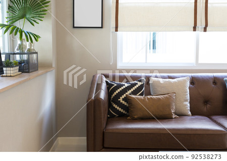 Light modern living room with brown leather couch and white, grey and green pillow on it. 92538273