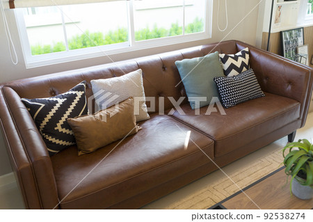 Light modern living room with brown leather couch and white, grey and green pillow on it. Light modern living room with brown leather couch and white, grey and green pillow on it. 92538274