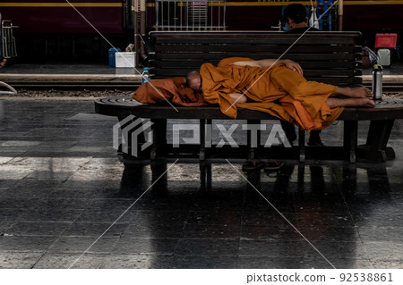 A monk is sleep on wooden chairs are waiting for trains in the area provided at Main railway station of Hua Lamphong. A monk is sleep on wooden chairs are waiting for trains in the area provided at Main railway station of Hua Lamphong. 92538861