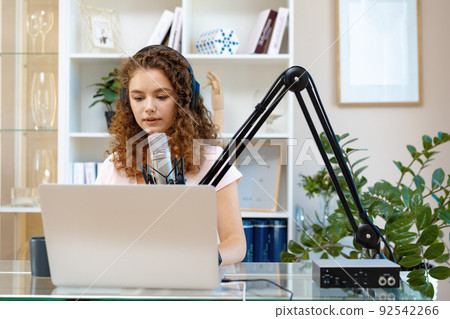Young curly female recording podcast from home and talking into a microphone 92542266