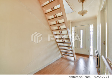 A spacious bright corridor with a wooden staircase and an entrance to the attic room with a window A spacious bright corridor with a wooden staircase and an entrance to the attic room with a window 92542771