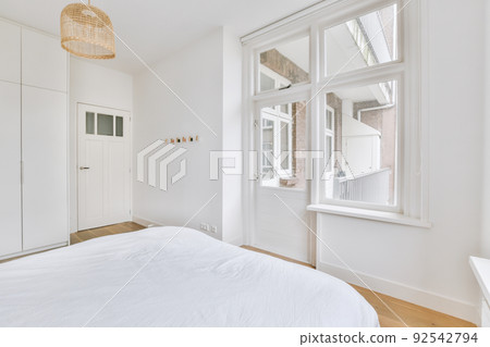 Home interior design of bedroom with bed and wooden wardrobe placed in corner near balcony door in modern apartment Home interior design of bedroom with bed and wooden wardrobe placed in corner near balcony door in modern apartment 92542794