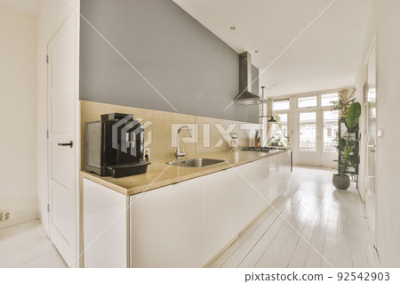 Fragment of interior of light narrow home kitchen with minimalist style white furniture with sink and stove 92542903