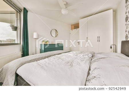 Home interior design of bedroom with bed and wooden wardrobe placed in corner near window in modern apartment Home interior design of bedroom with bed and wooden wardrobe placed in corner near window in modern apartment 92542949