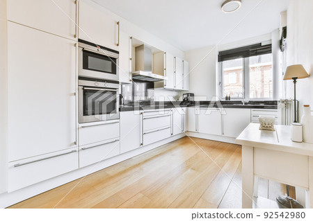 Fragment of interior of light narrow home kitchen with minimalist style white furniture with sink and stove Fragment of interior of light narrow home kitchen with minimalist style white furniture with sink and stove 92542980