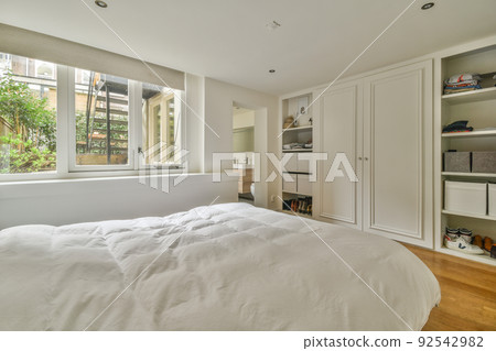 Home interior design of bedroom with bed and wooden wardrobe placed in corner near window in modern apartment 92542982