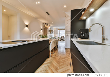 Modern minimalist style interior design of studio apartment with open black kitchen and dining zone with table and chairs illuminated by loft style lamp 92543112