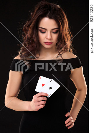 Young woman holding playing cards against a black background 92543226